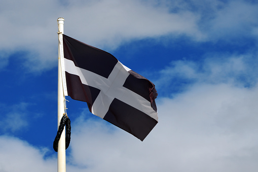 Marazion, Cornwall, England, UK: Saint Piran's Flag (Cornish: Baner Peran) is the flag of Cornwall. The flag is attributed to Saint Piran, a 5th-century Cornish abbot. But the white cross and black background design is also the coat of arms of the Saint-Perran (or Saint-Pezran) family from Cornouaille in Brittany, recorded from the 15th century.