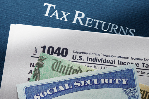 A United States Treasury government check and social security card rest on top of a United States federal 1040 tax return.