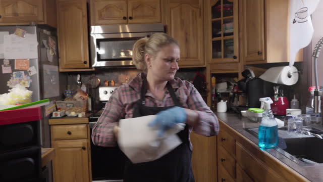 Female cleaning worker taking paper and starting her job behind the customer in the kitchen. Handheld camera motion