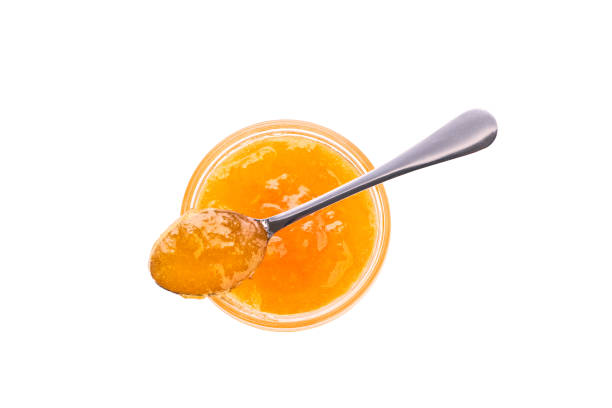 orange jam in jar with spoon isolated on white background, top view. Jar of orange confiture with spoon top view, isolated on white background.