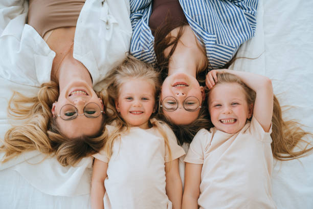 istock Top view on mother with daughters laying on bed looking at camera happily smiling enjoying time together, motherhood, childhood. Sisters posing at bedroom, cozy home. Blonde girls at home. 1815246426