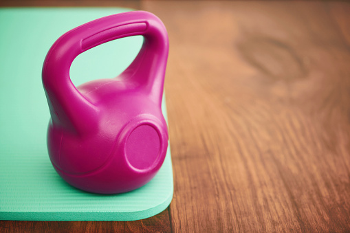 Pink kettle bell on a green yoga mat on a hardwood floor with copy space