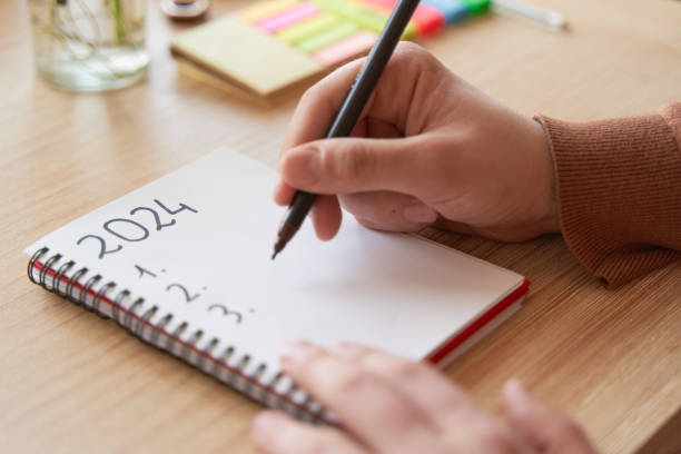 istock Young hands writing in notebook 2024 new year's resolutions index list over wooden table 1815261771