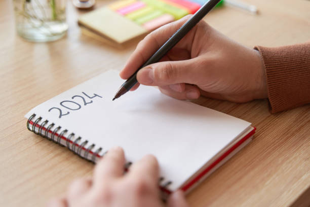 istock Young hands writing in notebook 2024 new year's resolutions and goals over wooden table 1815261773