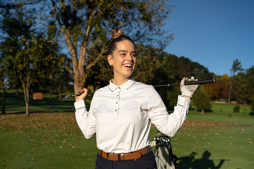 Happy young woman holding a golf club with two hands in the back and smiling