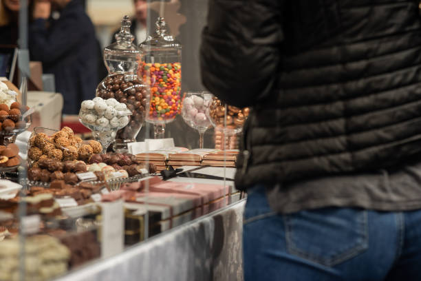 istock Person choosing different kinds of sweets on a display. Many chocolates on a fair, visible back of an unknown woman in jeans. 1815285133