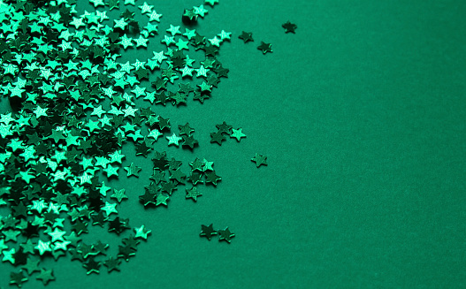 Green stars confetti on a green background. Christmas, New Year party festive backdrop with copy space. Green Golden Textured stars Glitter Background texture for Invitations, New Year, Merry Christmas, Birthday, Wedding, Valentines day.