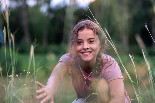 portrait of a teenage girl in a meadow peeking out from the grass, smiling