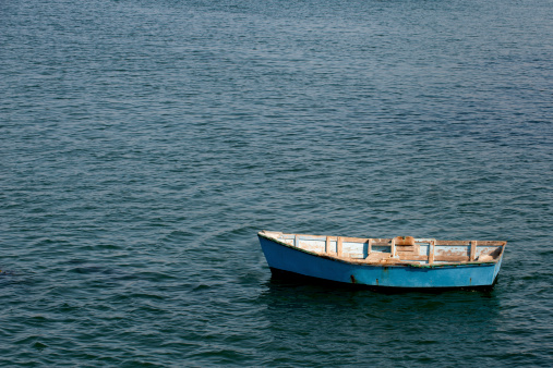 Photographic image of blue boat or dingy adrift in a large body of water