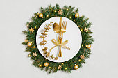 Beautiful Christmas table setting with gold cutlery, gold ornaments and festive wreath on white background. New Year party. Top view, flat lay.