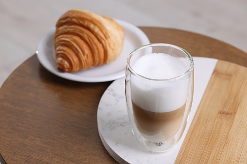 Aromatic latte macchiato in glass and croissant on wooden table