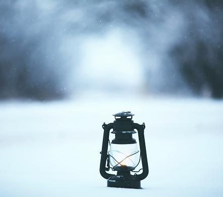 An old fashioned lantern in a snow drift with an archway of trees in the distance