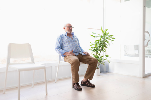 An older man waits in the reception area of a clinic for a rehabilitation and maintenance physiotherapy session