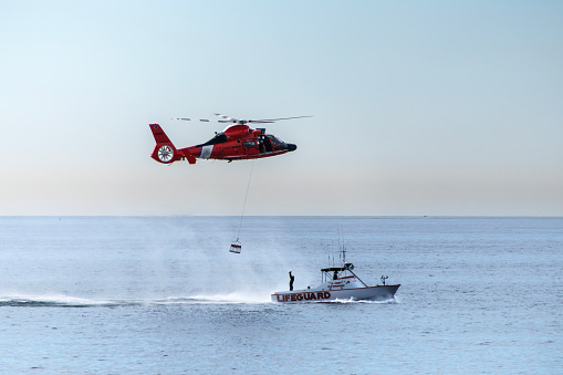 Los Angeles, California, USA - November 10, 2023;  US Coast Guard helicopter lowering a basket to a Los Angeles County Lifeguard boat.