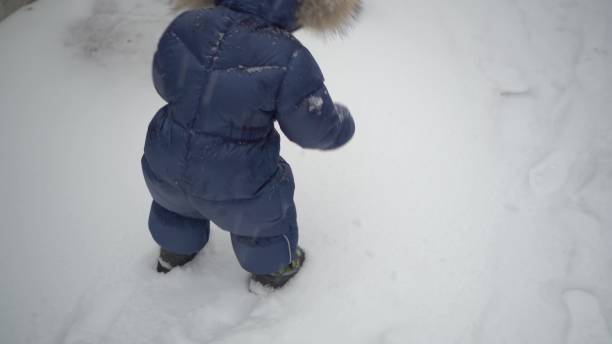 istock A small child walks through fresh snow. A boy in a down jacket steps on the snow and leaves footprints. Legs close up. 1815484271