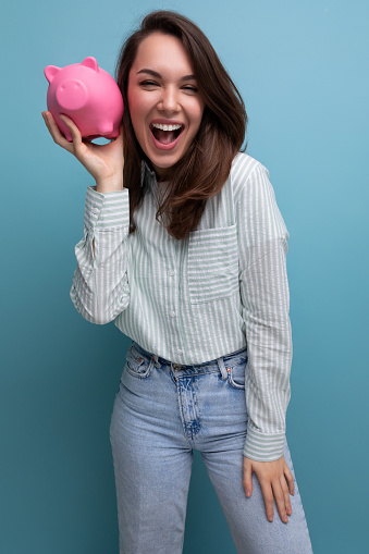 smiling attractive european brunette young lady keeps money in a pink piggy bank.