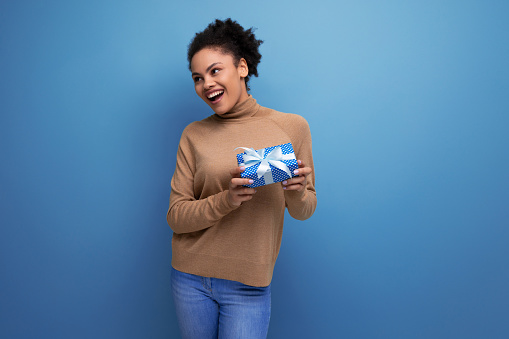 cheerful joyful young woman with dark skin and fluffy hair with gift box on isolated background with copy space.