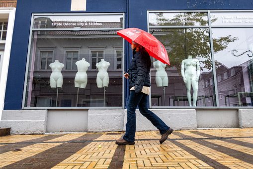Odense, Denmark Oct 30, 2023 A woman pedestrian with a red umbrella walks by large windows with female mannequins.