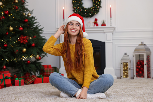 Beautiful young woman wearing Santa hat in room decorated for Christmas