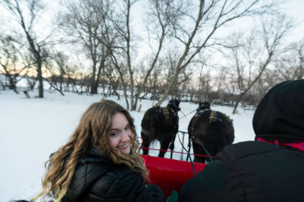 Blond woman smiles on a sleigh ride pulled by draft horses on a winter day, Minnesota