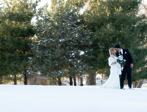 Wedding couple walk across snowy landscape in snowshoes, Minnesota