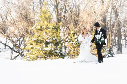 Wedding couple walk across snowy landscape in snowshoes, Minnesota