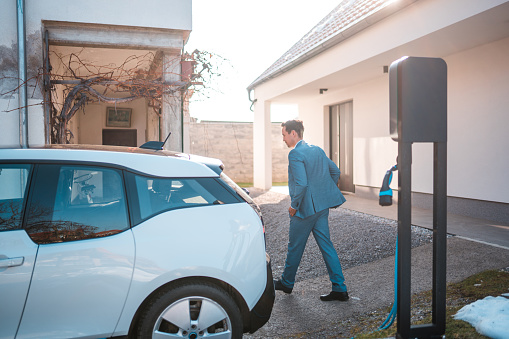 Daily routine. Asian man walking to his electric car on a beautiful morning. He looks stylish while wearing a blue suit.