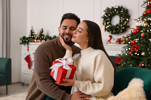 Beautiful young couple with Christmas gift at home