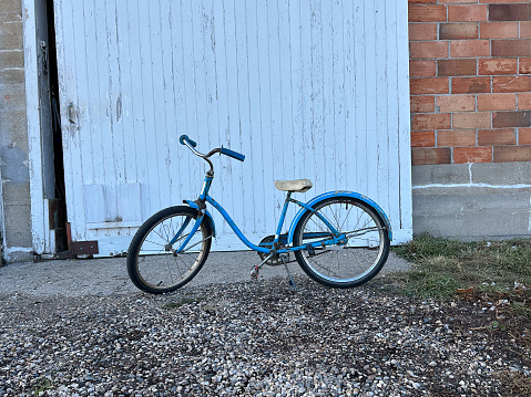 Old blue bicycle with metal basket parked beside a beige wall.