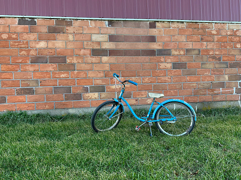 Old blue antique bike bicycle on green grass in front of old brick barn with old metal wagon wheels.