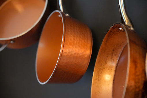 Detail of three copper pots hanging against a dark gray wall