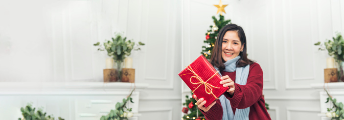 Banner Woman surprise got present gift box on christmas eve. Asian woman holding christmas gift box under xmas tree with smiling face. Happiness Women hands show gift. Merry christmas with copy space