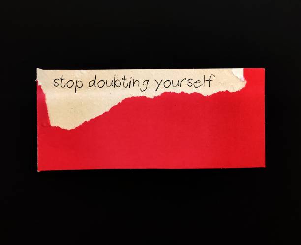 istock Torn red note on black background with handwritten text STOP DOUBTING YOURSELF, concept of self-doubt - lack of confidence  mindset that holds you back from succeeding leads to imposter syndrome or self-sabotage 1815693575