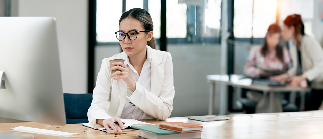 Thoughtfull young beautiful businesswoman in glasses working on laptop while sitting at her working place