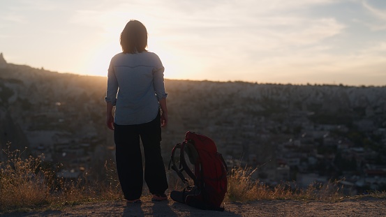 An Asian female tourist hiker is enjoying watching the sunset from up in the hill in Cappadocia Türkiye Turkey.