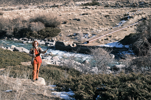 Cheerful woman of 45 is vlogging about her hiking on mountain riverbank in winter