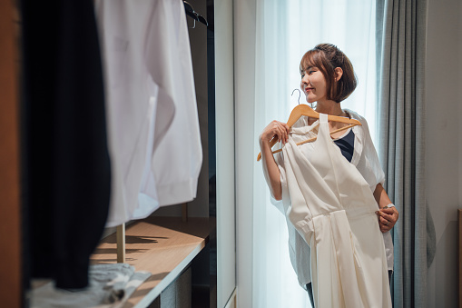 Happy Asian Woman Choosing a Dress at Home
