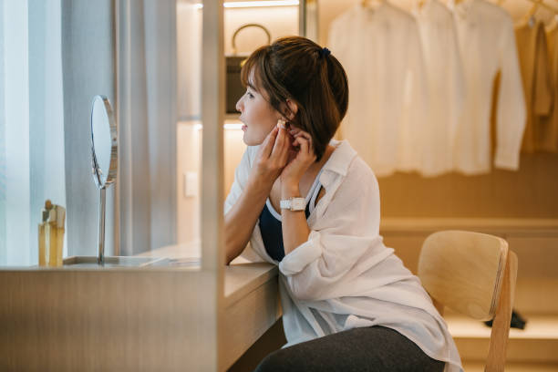 Happy Asian Woman Trying on Earrings in Front of the Mirror at Home, stock photo