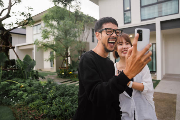 Happy Asian couples using smartphone video call for showing a new home