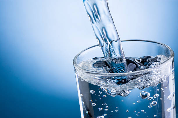 agua vertiendo en vidrio sobre fondo azul - agua purificada fotografías e imágenes de stock