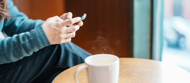 woman hand using smartphone during drinking hot Coffee or Tea in the morning. Concepts for business, online shopping, internet banking and money transfer