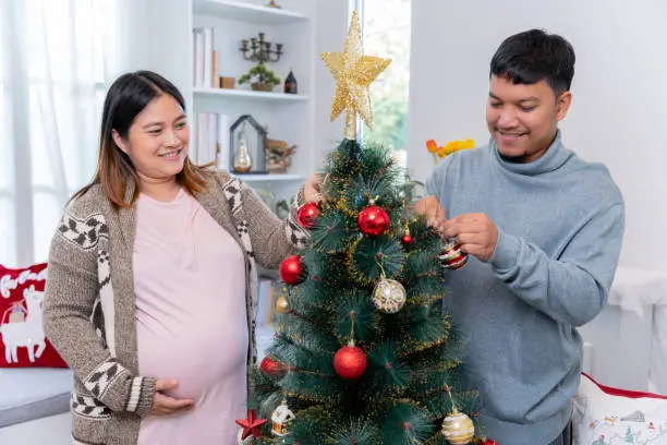 Asian pregnant woman with Thai husband at home. Christmas party and decoration. Family lifestyle on holiday.