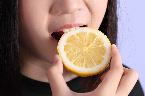 The Asian woman hand holding lemon in the purple background.