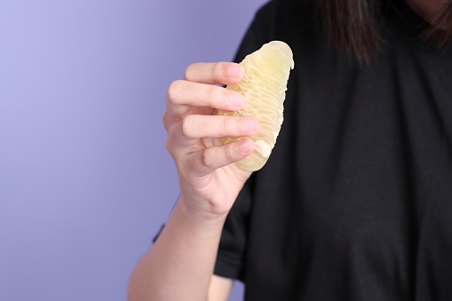 The Asian woman hand holding pomelo in the purple background.