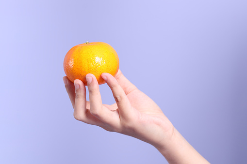 The Asian woman holding orange fruit on the purple background.