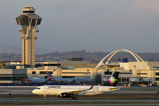 Los Angeles, California, United States: Volaris Airbus A320-233 with registration XA - VLK shown taxiing at LAX, Los Angeles International Airport. The Theme Building and air traffic control tower are shown.