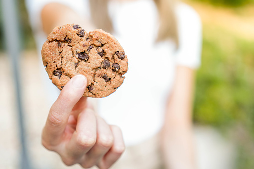 Closeup view of blurred young woman showing to camera delicious good looking chocolate chips cookie