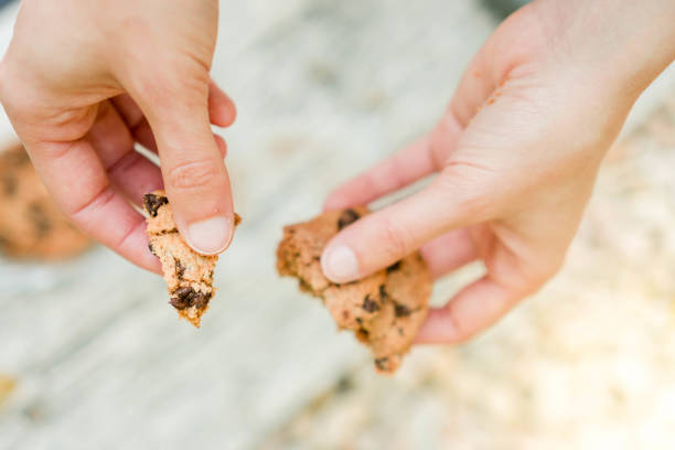 Close up top view of split chocolate cookie held by white hands in blurred background.