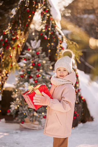 Little girl with a Christmas gift outdoors in winter on Christmas Eve.