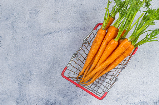 Small fresh orange carrots in a basket on a white background.